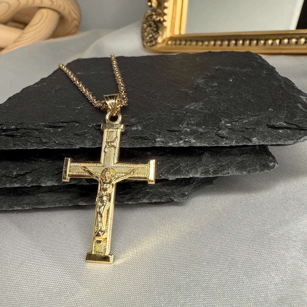Gold crucifix pendant on a black stone surface with a neutral background